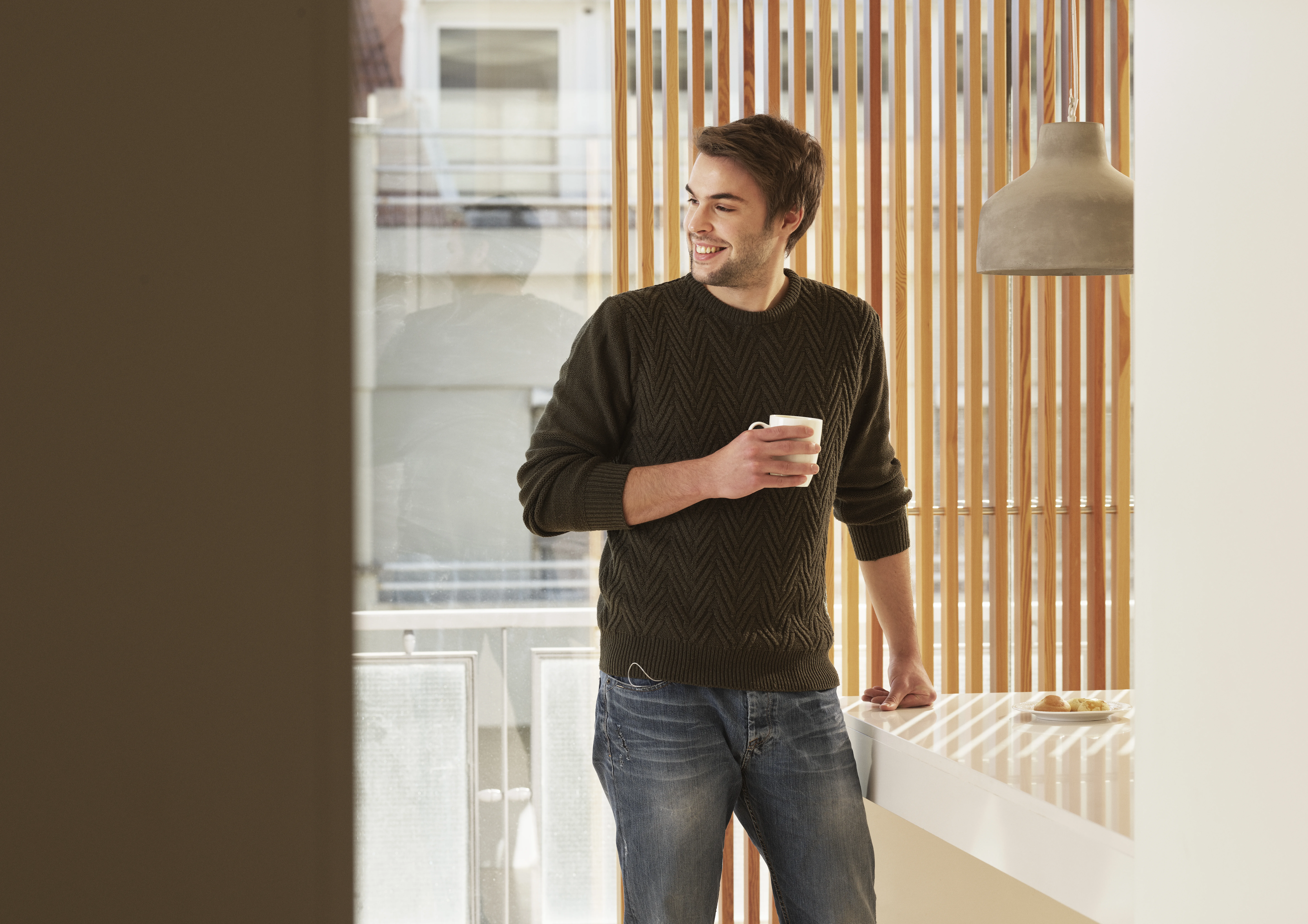 A man standing in front of a window holding a cup